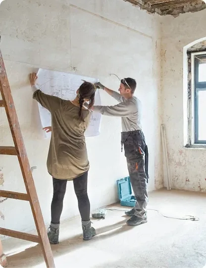 Zwei Handwerker markieren Baupläne an einer unverputzten Wand